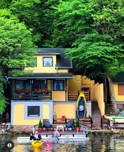 two people in kayaks in front of a house on the water at Kućica na Jezeru Ovčarsko-kablarska klisura Boat Access Only in Čačak