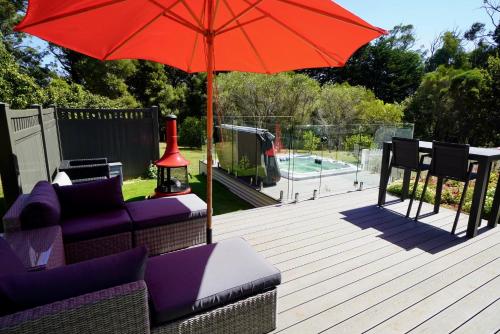 a patio with a red umbrella and chairs and a pool at Elegant bluestone cottage located at the Red Hill Peony Estate in Red Hill