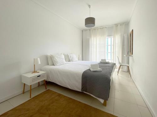 a white bedroom with a large bed and a night stand at CC - Casa da Costa in Costa Nova