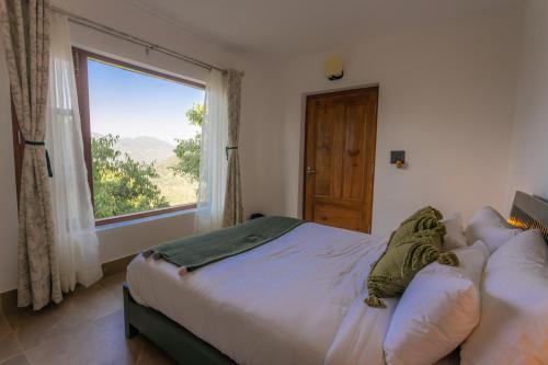 a bedroom with a bed and a large window at Seclude Ramgarh Willows in Rāmgarh