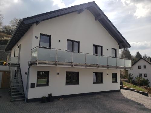 a white house with a balcony on top of it at Ferienwohnungen am Aeppelsberg in Volkesfeld