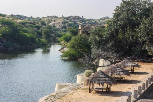 a river with tables and straw umbrellas next to a river at Brij Lakshmansagar, Pali - Small Luxury Hotels of the World in Raipur