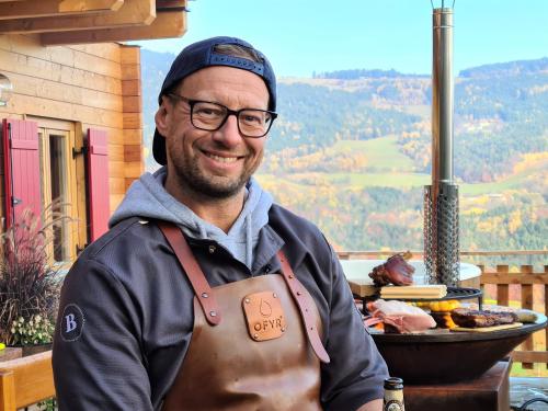 a man wearing an apron standing in front of a grill at Bergchalet mit Wellness-Oase, Natur Pur in Pöllauberg