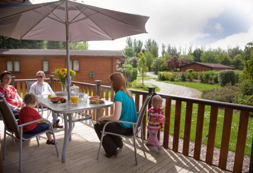 a family sitting at a table on a deck with an umbrella at Blairgowrie Holiday Park in Blairgowrie