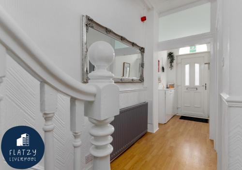 a white hallway with a staircase with a mirror at FLATZY - 6 bed Oasis Close to Football Stadiums in Liverpool
