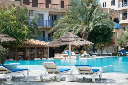 uma piscina com cadeiras e guarda-sóis ao lado de um hotel em Mike's Basilica apartment em Pafos