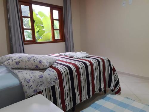 een kamer met een bed met een gestreepte deken en een raam bij Casa Aconchego visconde de Mauá in Itatiaia