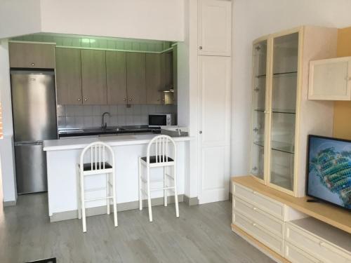 una cocina con 2 sillas blancas y una barra en Apartamento Los Cristianos Tres minutos Playa las vistas en Arona