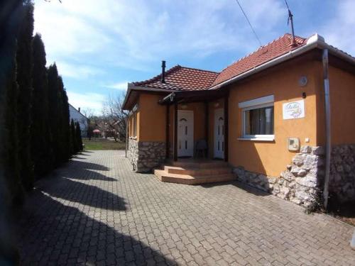 a small yellow house with a brick driveway at Bellis - Apartmanok in Szilvásvárad