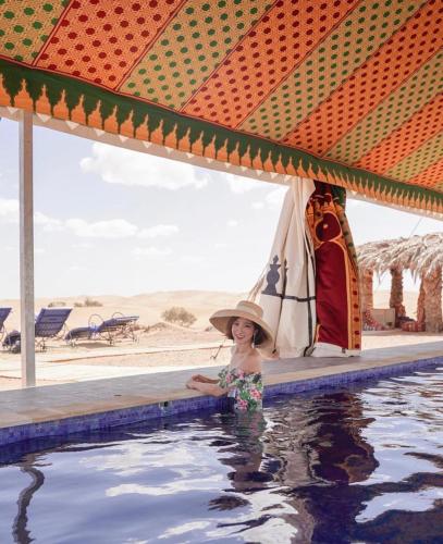 Una mujer con sombrero parada en una piscina en Desert Luxury Camp Morocco, en Merzouga