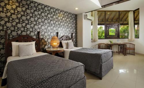 a bedroom with two beds and a table with a lamp at Taman Harum Cottages in Ubud