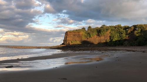 a beach with a cliff in the distance with the ocean at @Taradise-Opunake - eco-friendly Coastal hideaway in Opunake