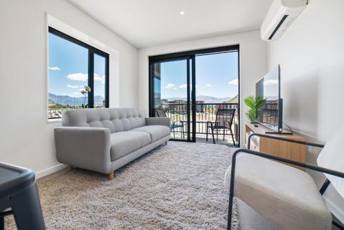 a living room with a couch and a tv and windows at Toru Top Floor Apartment - Brand New & Convenient in Queenstown