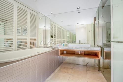 La salle de bains blanche est pourvue d'une baignoire et d'un lavabo. dans l'établissement Unit 8 Plantation Resort Rainbow Beach, à Rainbow Beach