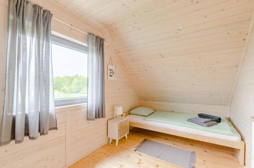 a small bed in a wooden room with a window at Biale Domki Kopalino in Kopalino