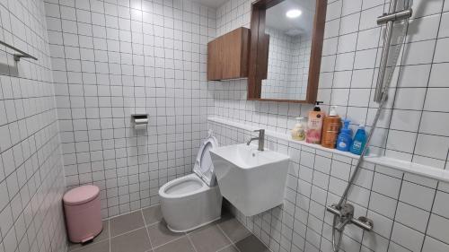 a white tiled bathroom with a toilet and a sink at Jungle guesthouse in Danyang