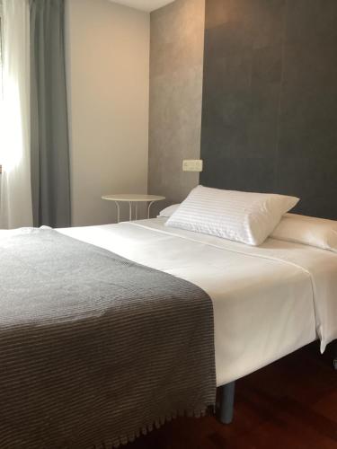 a bedroom with a white bed with a table at Saudade Hostal Cafetería in A Coruña