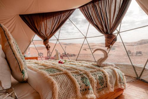 uma cama num quarto com uma grande janela em Desert Luxury Camp em Merzouga