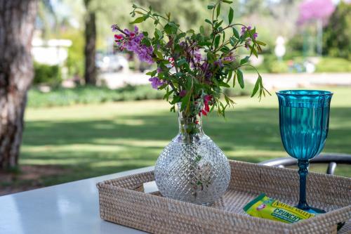 a vase with purple flowers on a table with a glass at Kibbutz Malkiya Travel Hotel in Malkiyya