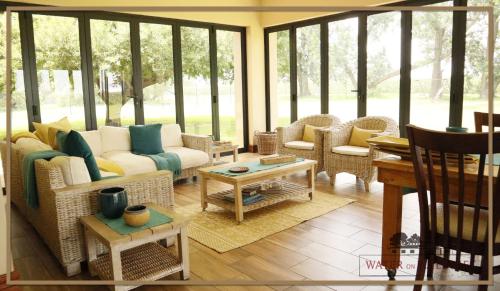 a living room with wicker furniture and glass windows at Water on Waldrift Guesthouse in Vereeniging