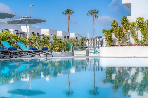 a swimming pool with chairs and an umbrella and palm trees at Rosamar Apartamentos in Puerto del Carmen