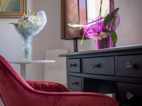 una silla roja y un jarrón con flores en un tocador en Ego' Residence Ferrara, en Ferrara