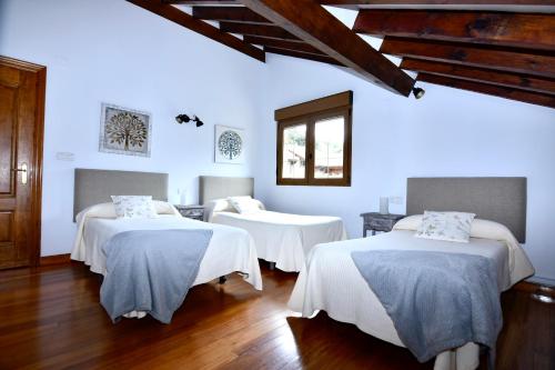 3 camas en una habitación con paredes blancas y suelo de madera en Apartamentos Rurales Valverde en Potes