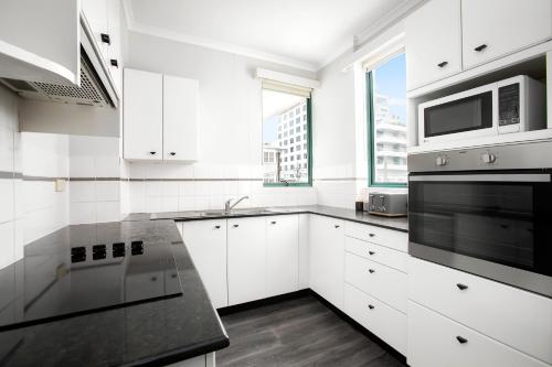 a white kitchen with a microwave and a stove at The Coogee View Beachfront Serviced Apartments in Sydney