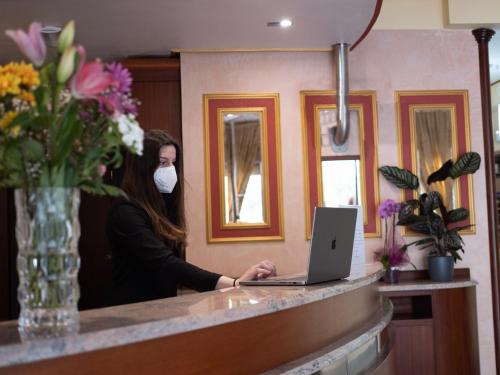 a woman in a mask sitting at a counter with a laptop at EGO' Residence Ferrara in Ferrara