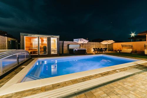 a swimming pool in front of a house at night at Tópart Apartmanok ***** Algyő in Algyő