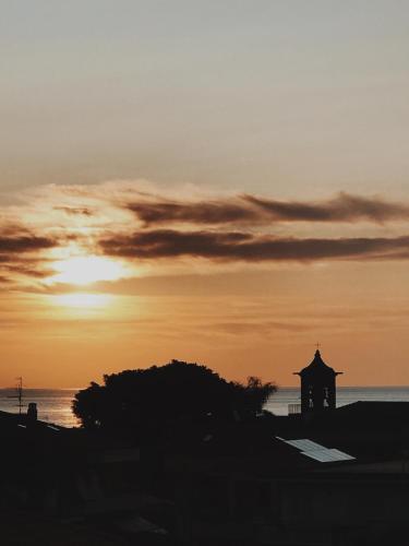 a sunset over the ocean with a building on the beach at Path House - Etna & Sea View in Riposto