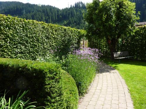a garden with a bench next to a hedge and flowers at Haus Christopherus in Klösterle am Arlberg
