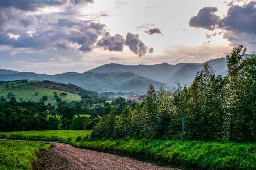 a dirt road in a field with mountains in the background at The Crested Crane Bwindi Hotel in Rugando