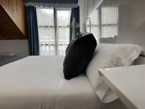 a black pillow sitting on a white bed with a window at Hotel Avelina in Cangas de Onís