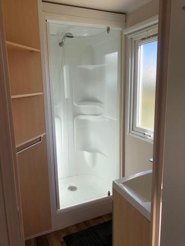 La salle de bains est pourvue d'une douche blanche et d'une fenêtre. dans l'établissement Mobilhome A16 Au phare d Opale, à Le Portel
