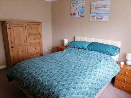 a bedroom with a bed with blue sheets and a wooden cabinet at Inviting light and airy 3-Bed Apartment in Wick in Wick