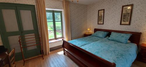 een slaapkamer met een bed met een blauw dekbed en een raam bij Chambres d'hôtes a l'étang d'Yonne in Arleuf