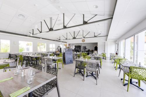 une salle à manger avec tables, chaises et fenêtres dans l'établissement Vent d'Eden Park Hôtel, à Saint-Hilaire-de-Riez