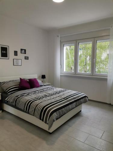 a white bedroom with a large bed with purple pillows at Apartman Maki in Sombor