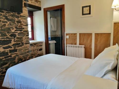 1 dormitorio con cama blanca y pared de piedra en Las Rocas, en Vega de Valcarce