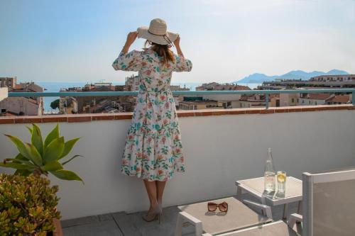 a woman in a dress and hat standing on a balcony at BW Premier Collection Mondial in Cannes