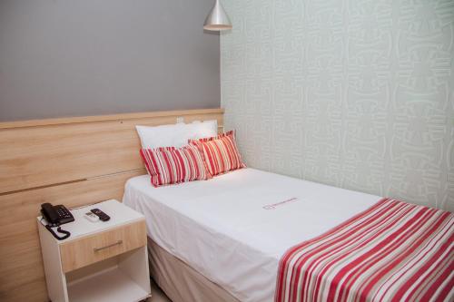 a small bedroom with a bed and a phone on a night stand at Grande Hotel Ipatinga in Ipatinga