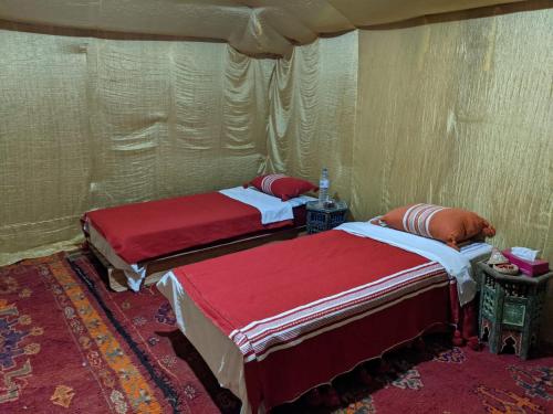 two beds in a room with red sheets at Sahara Desert Experience camp in Merzouga