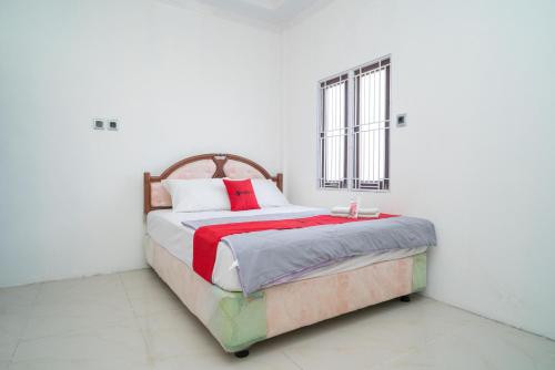 a white bedroom with a bed with red pillows at RedDoorz Syariah near Jalan A Yani KM 8 Citraland in Banjarmasin