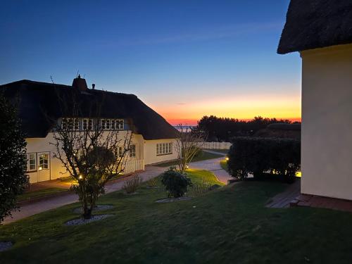 ein Haus mit einem Strohdach und einem Sonnenuntergang im Hintergrund in der Unterkunft Haus Amanda in Norddorf