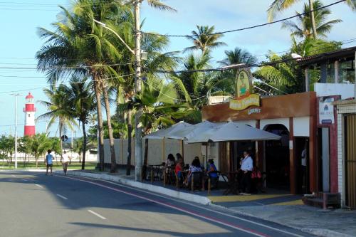 un groupe de personnes assis à l'extérieur d'un restaurant avec un phare dans l'établissement FAROL BEACH Apartamentos & Suítes, à Salvador