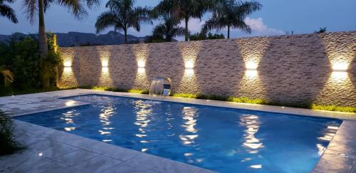 a swimming pool in front of a stone wall with lights at ALMA VILLAGE CASA CAMPESTRE MARIQUITA in Guayabal