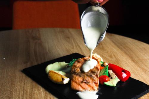a spoon is pouring white sauce onto a plate of food at Adagio Jeddah City Center in Jeddah