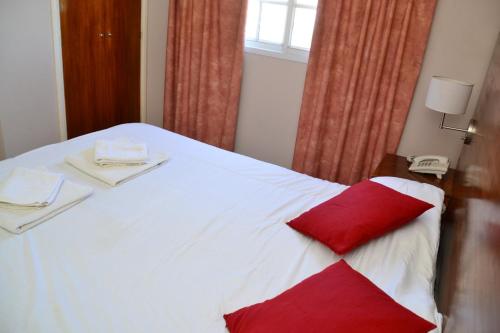 a white bed with a red pillow on it at Hotel Paucam in Santa Teresita
