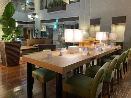 a large wooden table with green chairs and lamps at CYPRESS HOTEL Nagoya-eki Mae in Nagoya